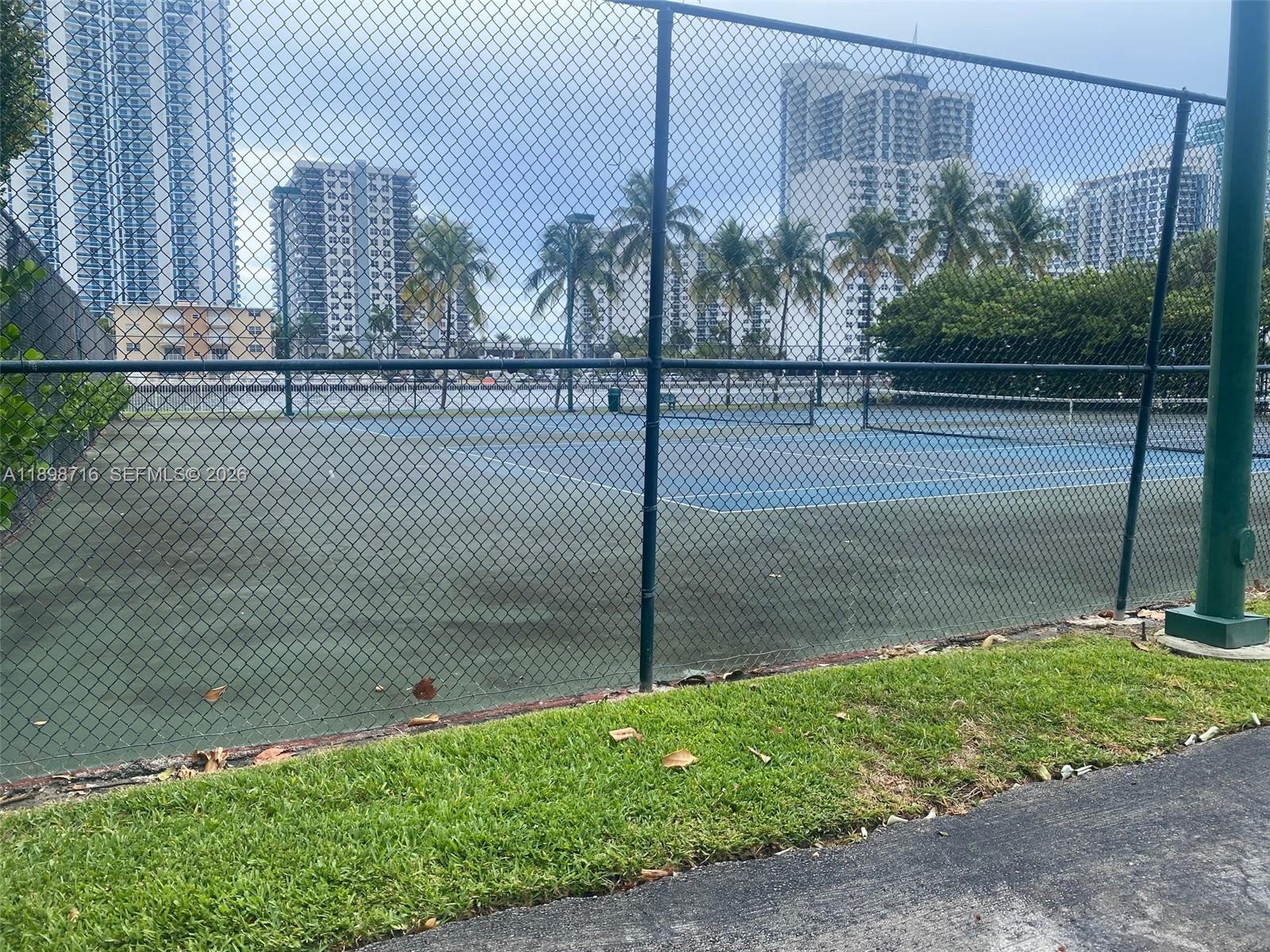 A fenced tennis court sits outdoors in front of several high-rise apartment buildings — 1000 Parkview Dr # 427, Hallandale Beach FL 33009, HALLANDALE BEACH, FL