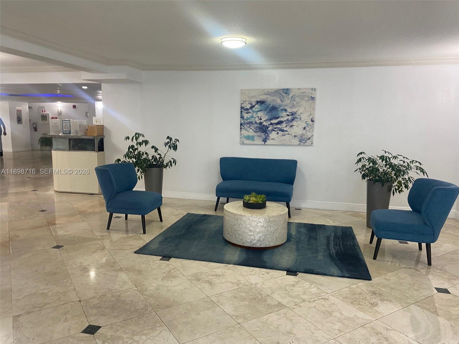 A spacious, tiled lobby features blue armchairs, a round coffee table, and potted plants — 1000 Parkview Dr # 427, Hallandale Beach FL 33009, HALLANDALE BEACH, FL