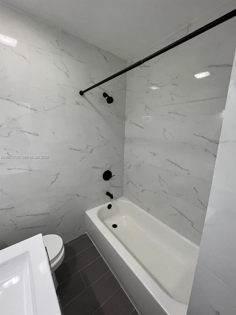 A bathroom features a white bathtub, black fixtures, and white marble-patterned wall tiles — 2640 NE 215th St # 2640, Miami FL 33180, MIAMI, FL