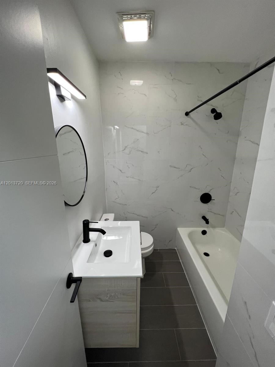 A modern bathroom features a white vanity, a bathtub with black fixtures, and marble-patterned tiles — 2640 NE 215th St # 2640, Miami FL 33180, MIAMI, FL
