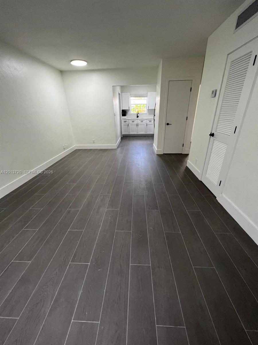 A room with dark wood-look tile flooring leads to a white kitchen in the background — 2640 NE 215th St # 2640, Miami FL 33180, MIAMI, FL