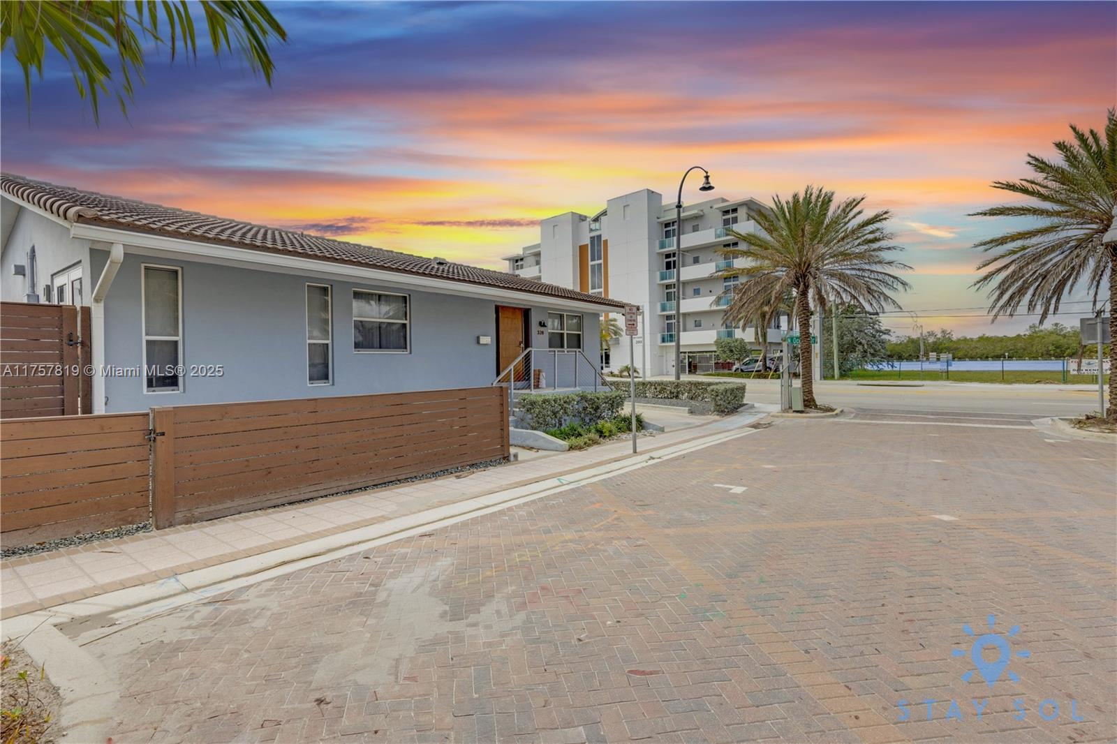 A light blue single-story house with a wooden fence stands next to a paved street — 328 Missouri St, Hollywood FL 33019, HOLLYWOOD, FL
