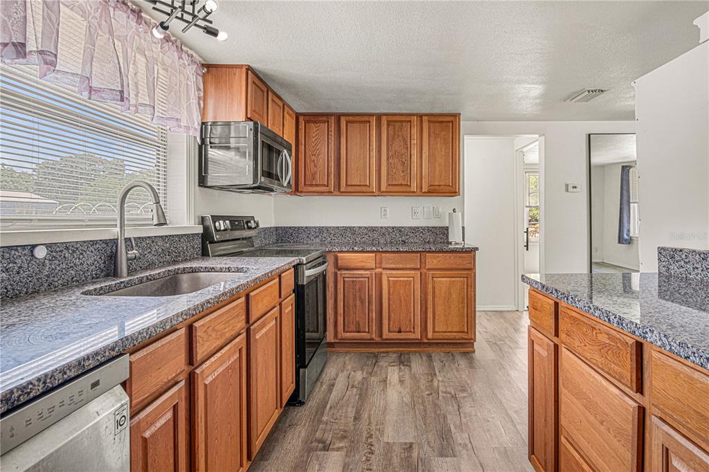 A kitchen features wood cabinets, granite countertops, stainless steel appliances, and wood-look flooring — 3545 PERKINS AVENUE, MOUNT DORA, FL