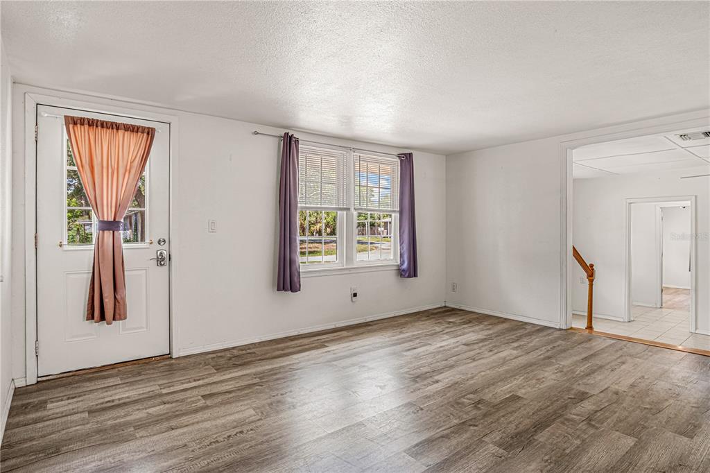 A living room with wood-look flooring, white walls, a front door, and a window — 3545 PERKINS AVENUE, MOUNT DORA, FL