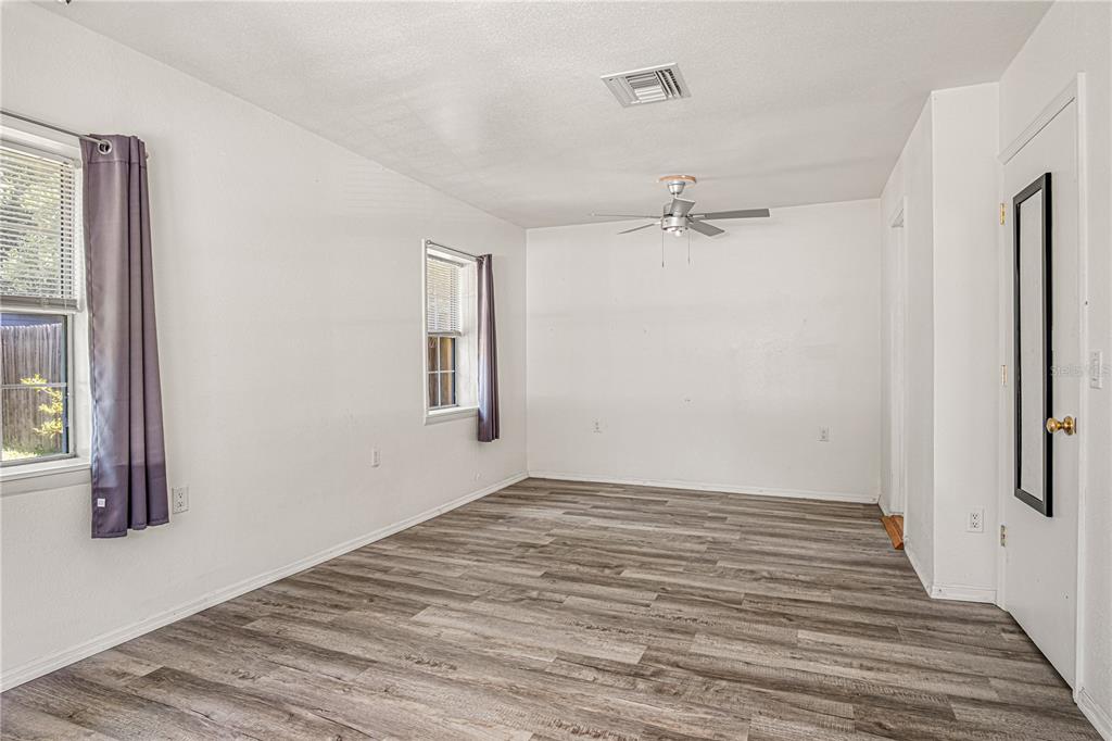 An empty room features gray wood-look flooring, white walls, two windows, and a ceiling fan — 3545 PERKINS AVENUE, MOUNT DORA, FL