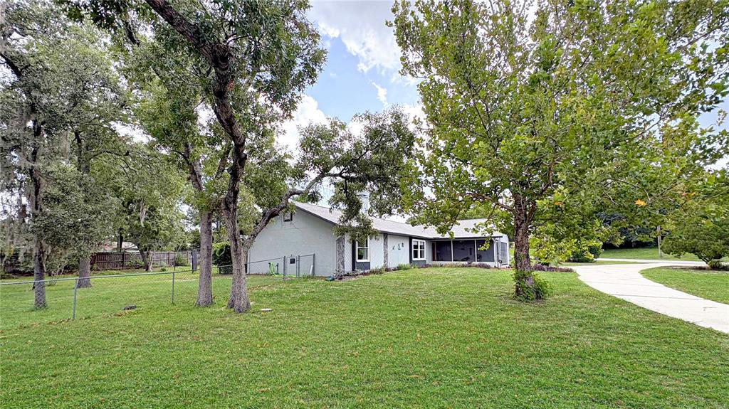 A light-colored single-story house sits on a grassy lot with mature trees and a driveway — 1420 SOMERSET AVENUE, SPRING HILL, FL