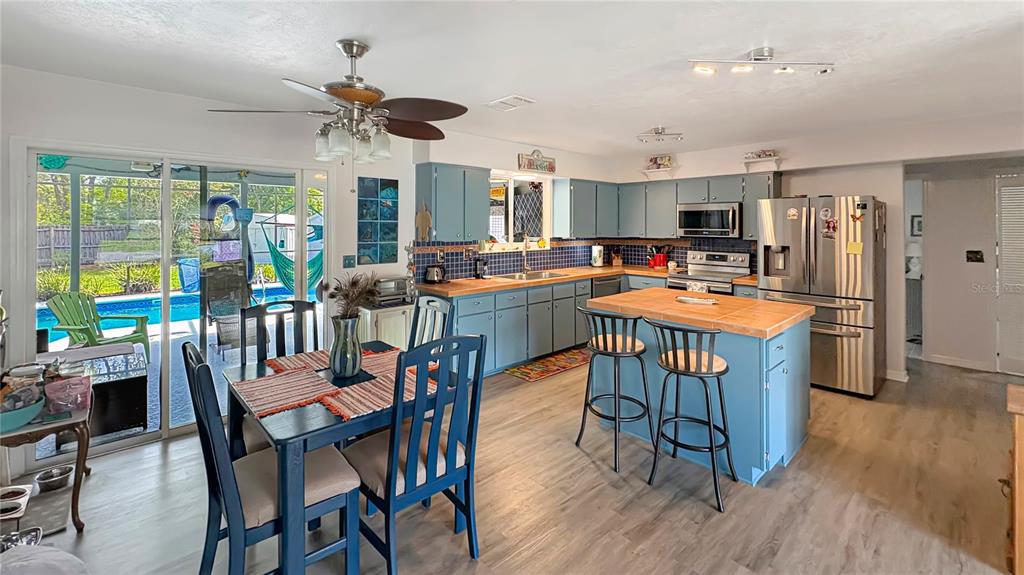 A kitchen with blue cabinets, a wooden island, and a dining area overlooking a pool — 1420 SOMERSET AVENUE, SPRING HILL, FL