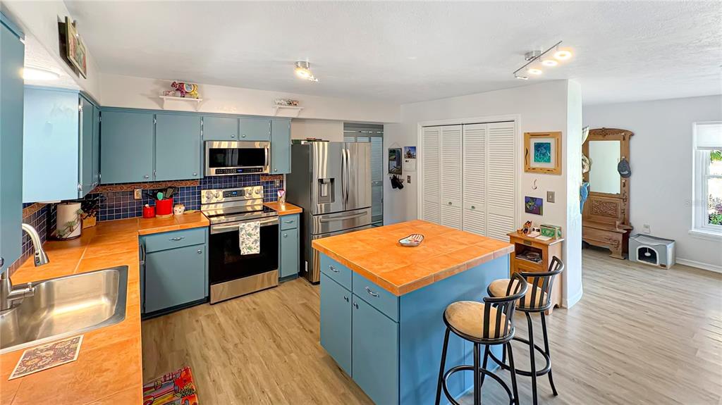A kitchen features blue cabinets, orange tiled countertops, a center island, and stainless steel appliances — 1420 SOMERSET AVENUE, SPRING HILL, FL