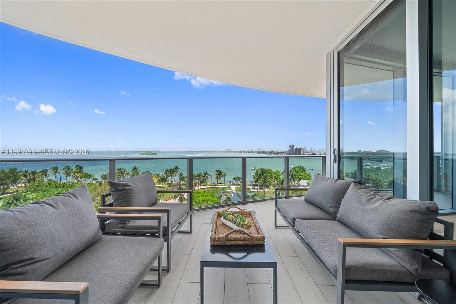 A balcony with gray outdoor furniture overlooks a bay and a park — 488 NE 18th St # 715, Miami FL 33132, MIAMI, FL