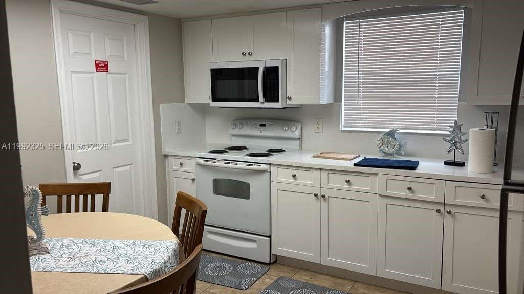 A kitchen features white cabinets, white appliances, and a small dining table with chairs — 1120 NE 24th Ave # 2, Pompano Beach FL 33062, POMPANO BEACH, FL