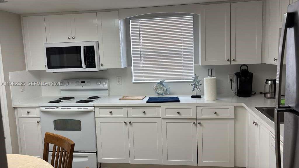 A kitchen features white cabinets, white appliances, a window with blinds, and white countertops — 1120 NE 24th Ave # 2, Pompano Beach FL 33062, POMPANO BEACH, FL