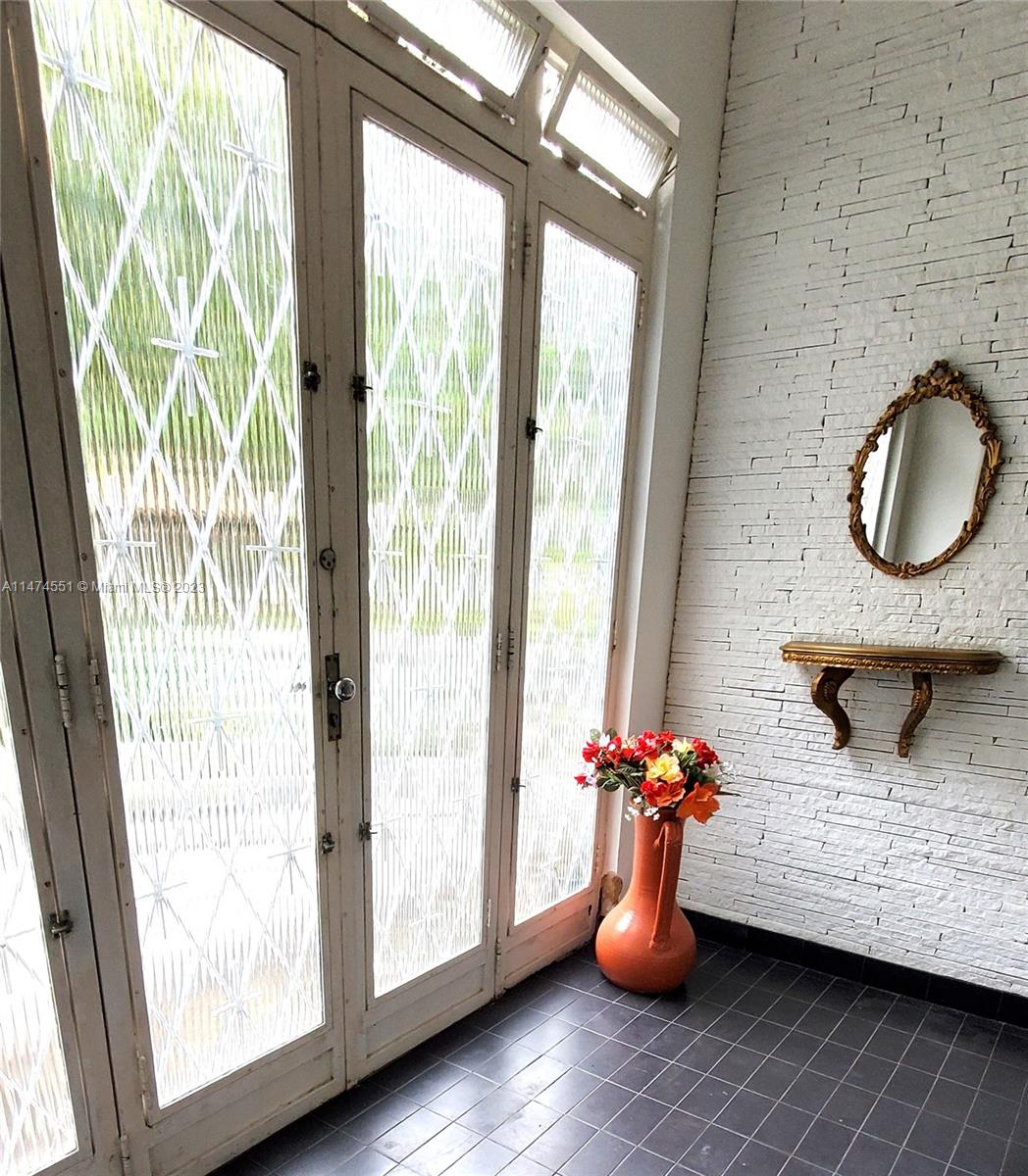 An entryway features a white brick wall, a small mirror, a console table, and glass doors — 311 MOSELA, FL 25675-481, FL