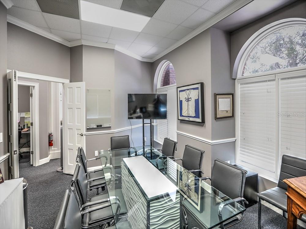 A conference room features a glass-topped table, black chairs, a wall-mounted television, and arched windows — 705 DOUGLAS AVENUE, ALTAMONTE SPRINGS, FL