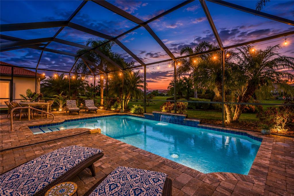 A screened-in swimming pool with a waterfall feature and patio furniture at sunset — 10233 LOCH LOMOND DRIVE, BRADENTON, FL