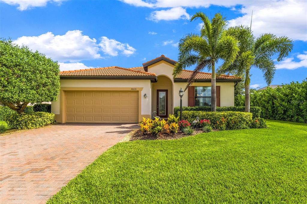 A single-story house with a tan stucco exterior, tile roof, and a paved driveway — 10233 LOCH LOMOND DRIVE, BRADENTON, FL