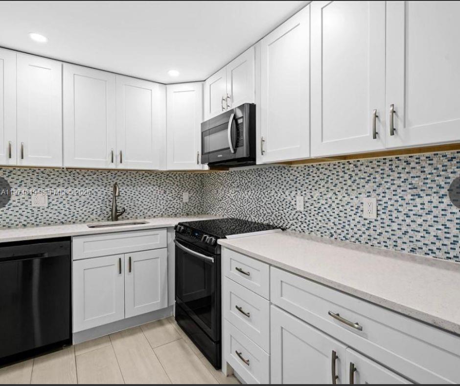 A kitchen features white cabinets, black appliances, a light countertop, and a blue mosaic backsplash — 1505 N Riverside Dr # 505, Pompano Beach FL 33062, POMPANO BEACH, FL