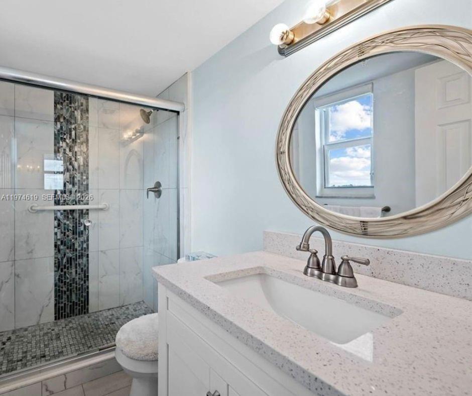 A bathroom features a white vanity with a speckled countertop, an oval mirror, and a shower — 1505 N Riverside Dr # 505, Pompano Beach FL 33062, POMPANO BEACH, FL