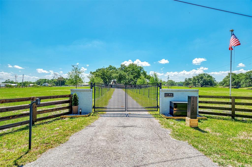 A gated driveway entrance features a white brick pillar, a metal fence, and an American flag — 10433 SW JERNIGAN STREET, ARCADIA, FL