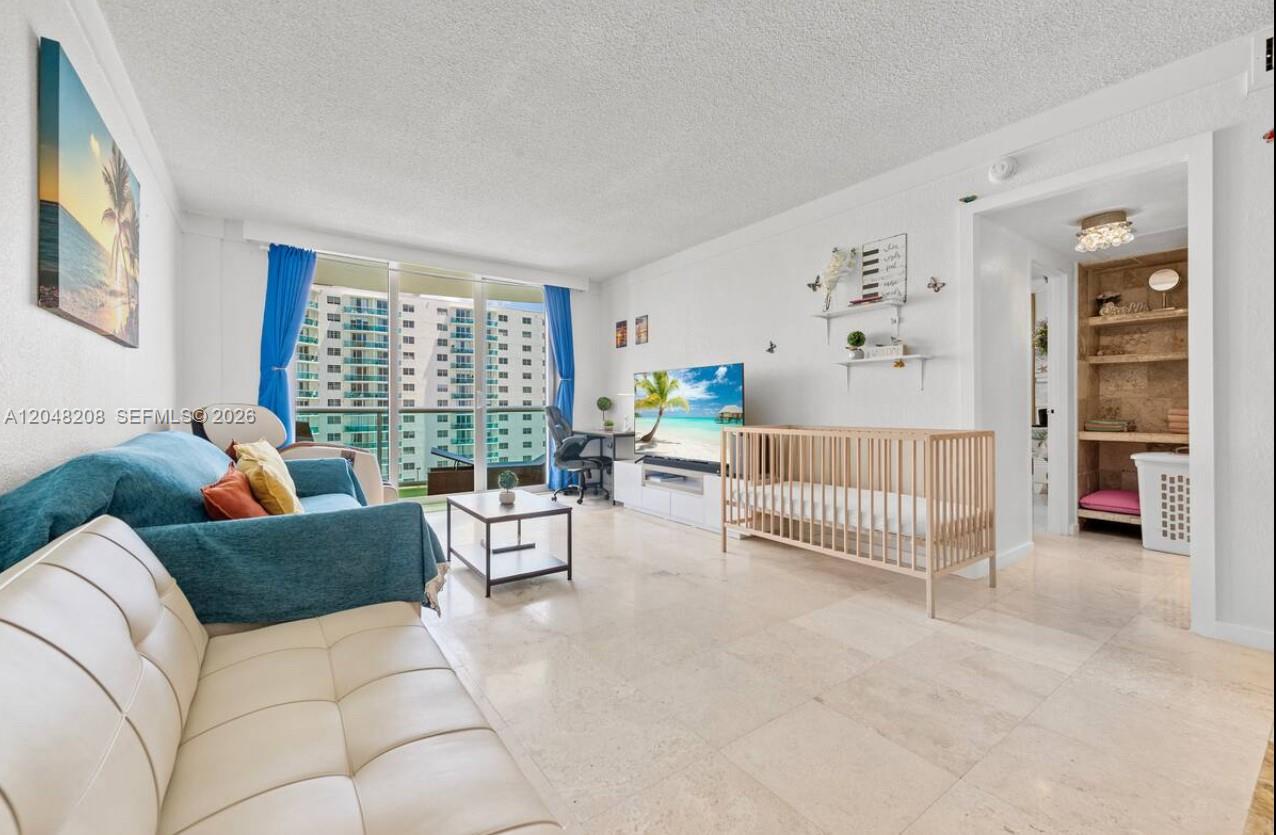A living room features a blue sofa, a crib, a television, and tile flooring — 3901 S Ocean Dr # 9B, Hollywood FL 33019, HOLLYWOOD, FL