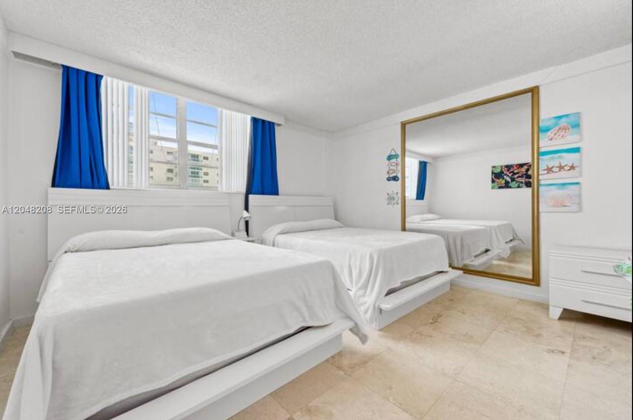 A bedroom features two white beds, a large wall mirror, and blue window curtains — 3901 S Ocean Dr # 9B, Hollywood FL 33019, HOLLYWOOD, FL