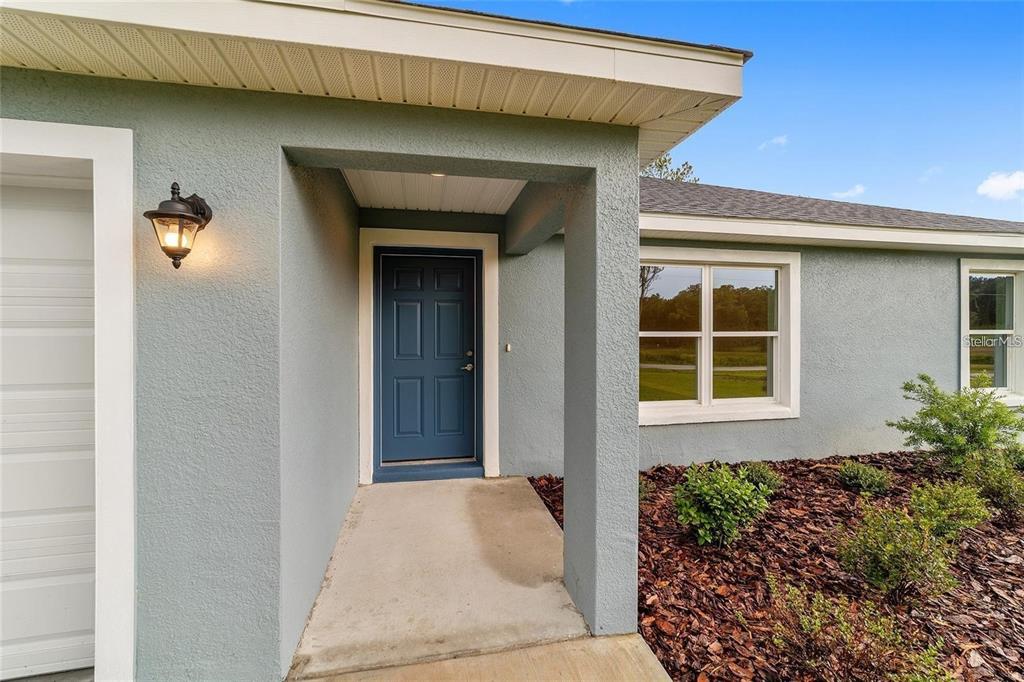 A blue front door is recessed under a covered entryway next to a garage — 7729 SW 146 LANE, OCALA, FL