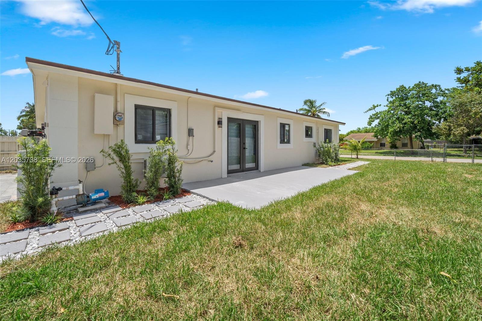 The exterior of a beige house features a concrete patio, sliding glass doors, and landscaping — 1944 NE 2nd Ave, Pompano Beach FL 33060, POMPANO BEACH, FL