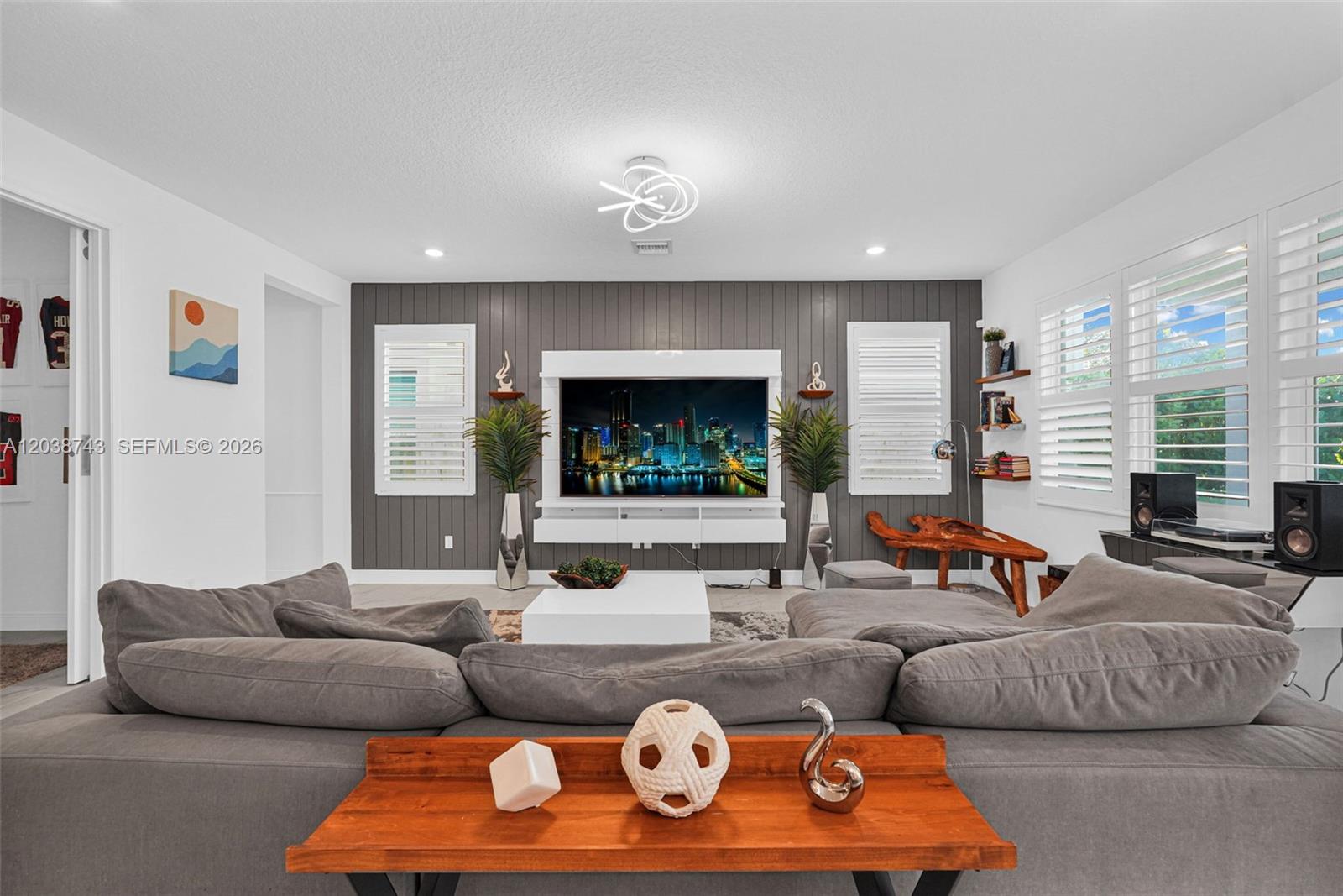 A living room features a gray shiplap accent wall with a mounted television and sectional — 4091 Pelicano Way # 4091, Deerfield Beach FL 33064, DEERFIELD BEACH, FL