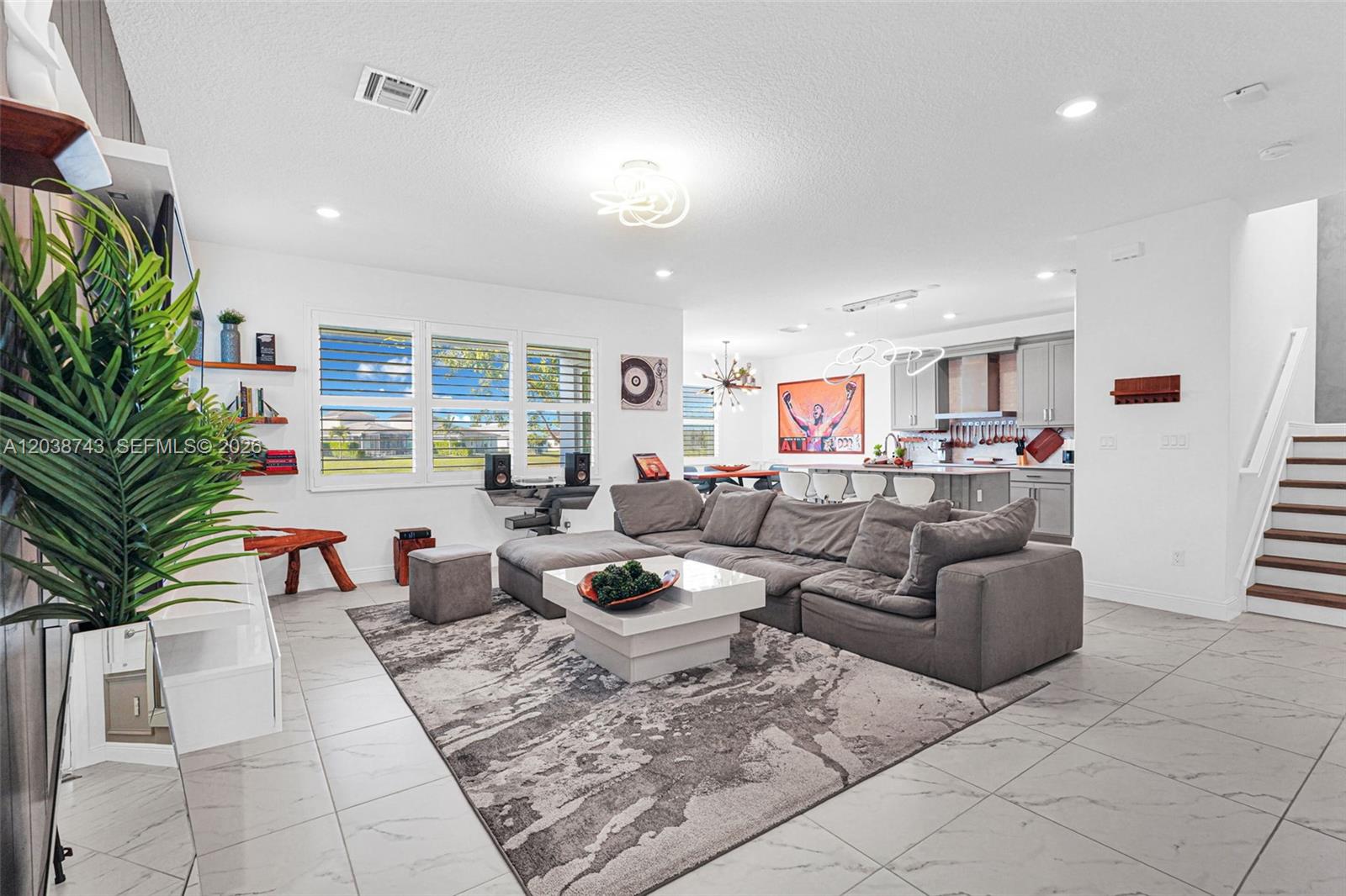A modern open-concept living room features a gray sectional sofa, tile flooring, and kitchen — 4091 Pelicano Way # 4091, Deerfield Beach FL 33064, DEERFIELD BEACH, FL