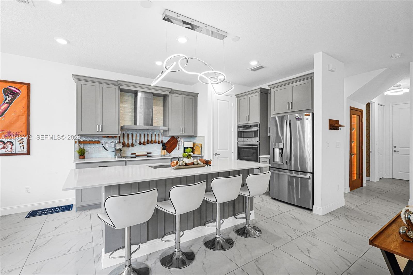 A modern kitchen features gray cabinets, a white island with bar stools, and stainless appliances — 4091 Pelicano Way # 4091, Deerfield Beach FL 33064, DEERFIELD BEACH, FL