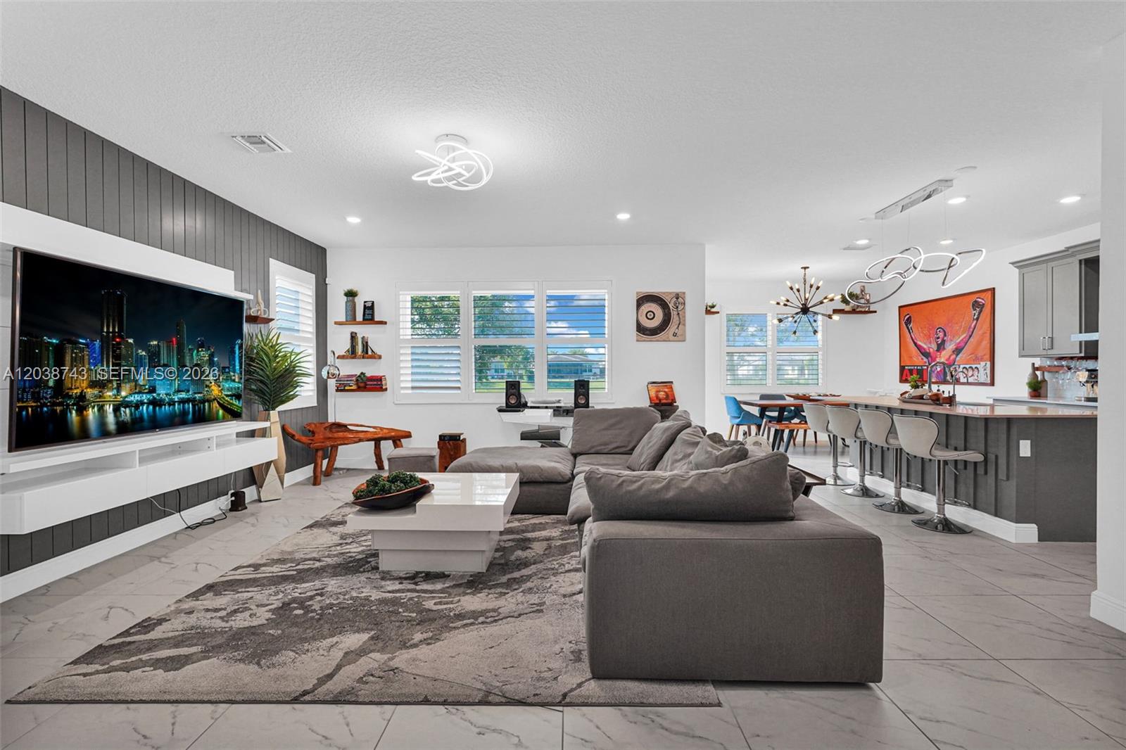 A modern open-concept living room and kitchen featuring a large sectional, television, and island seating — 4091 Pelicano Way # 4091, Deerfield Beach FL 33064, DEERFIELD BEACH, FL