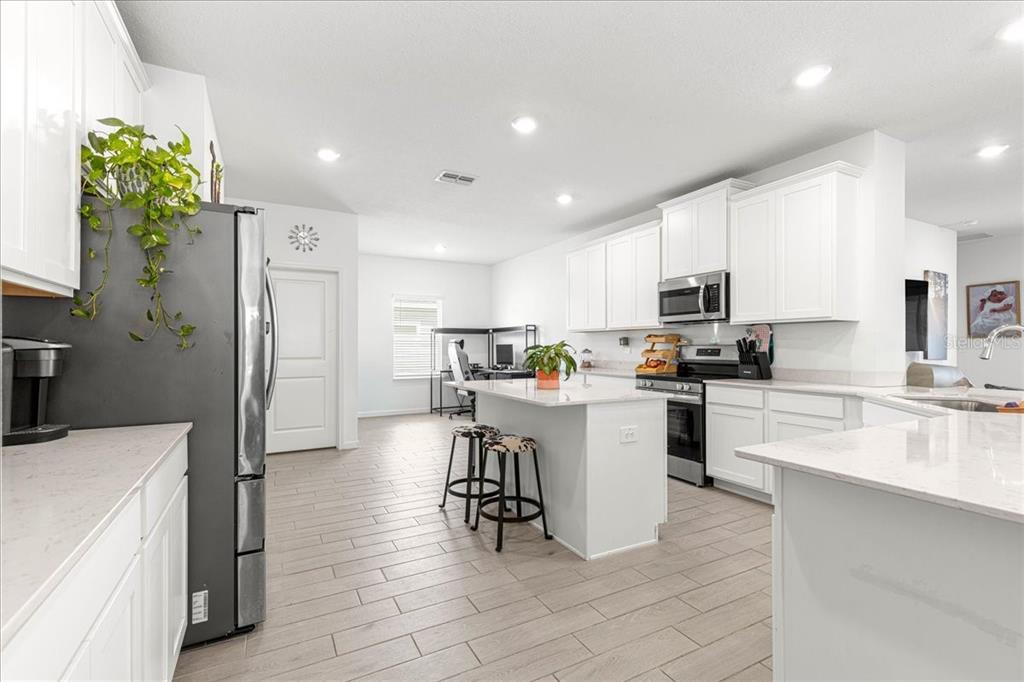 A modern kitchen features white cabinetry, a central island with bar stools, and light flooring — 3889 NE 33RD TERRACE, OCALA, FL