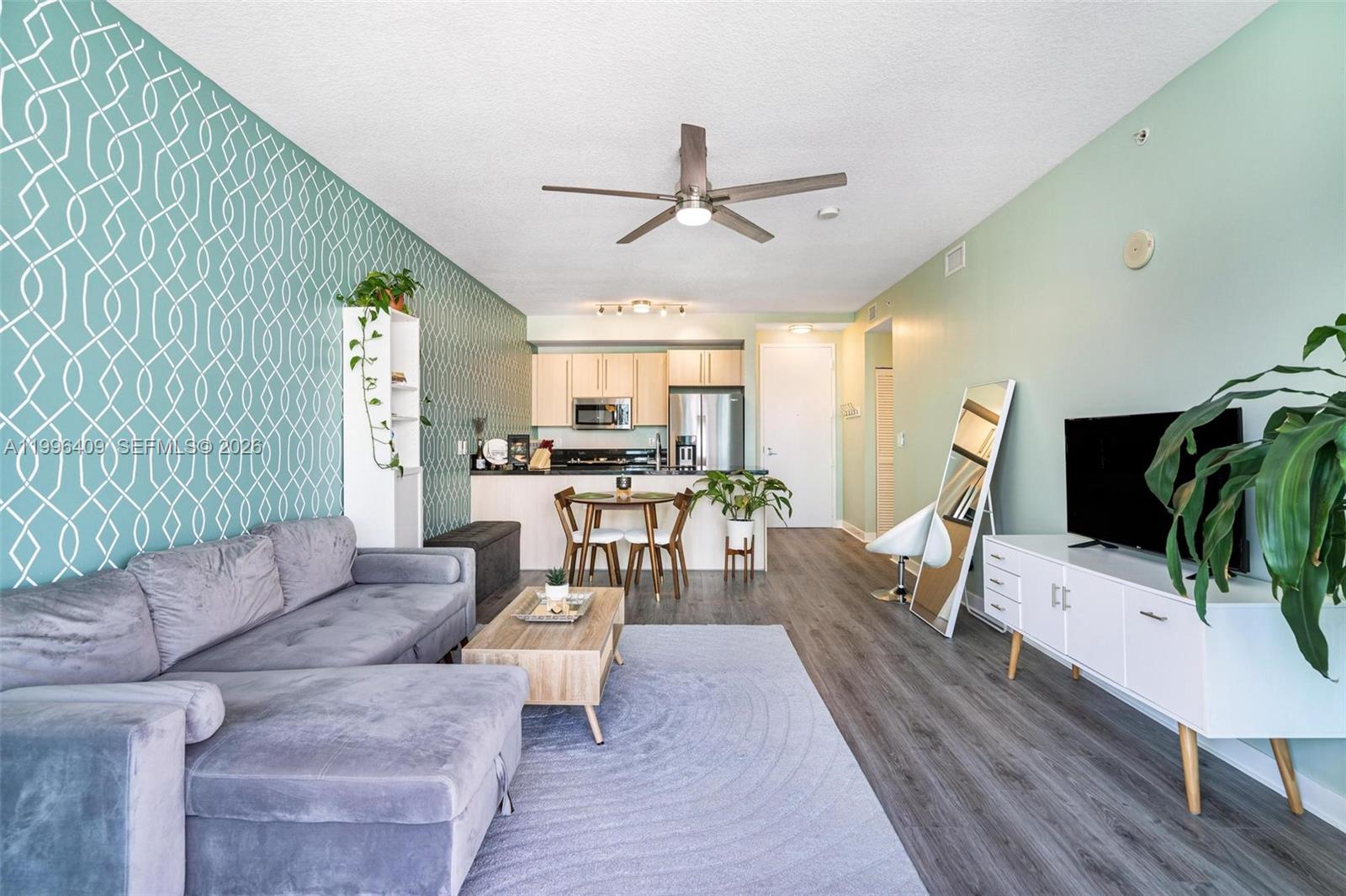 A living room features a gray sectional sofa, patterned wallpaper, and an open kitchen area — 1111 SW 1st Ave, Miami FL 33130, MIAMI, FL