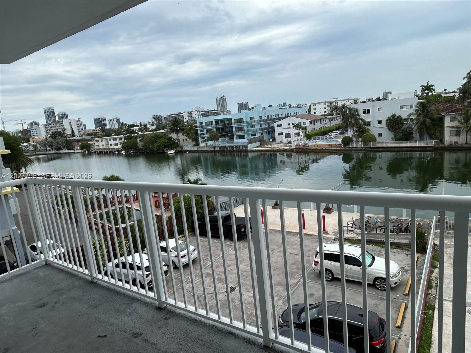 A balcony view overlooks a canal, a parking lot with several cars, and distant city buildings — 110 S Shore Dr # 4E, Miami Beach FL 33141, MIAMI BEACH, FL