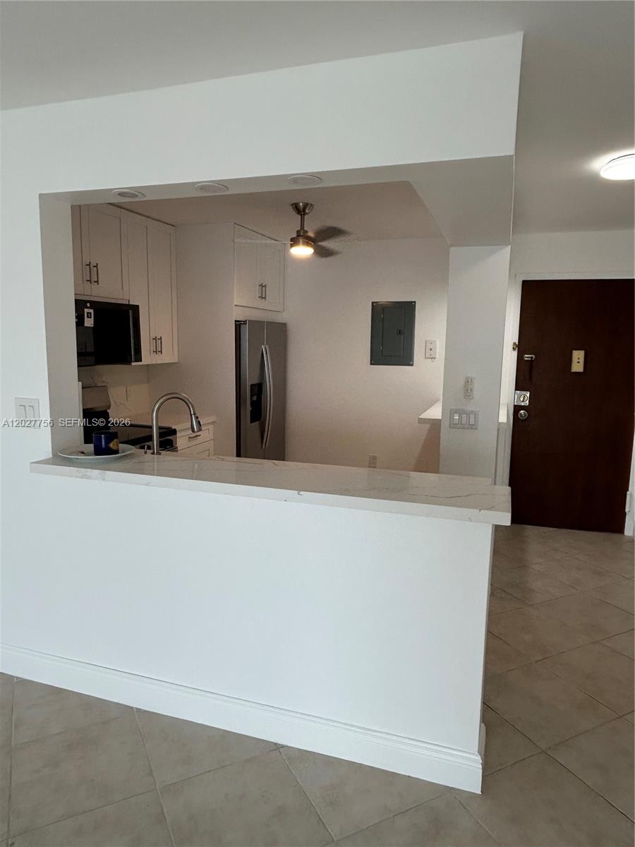 A kitchen with white cabinets and a breakfast bar overlooks a tiled entryway — 110 S Shore Dr # 4E, Miami Beach FL 33141, MIAMI BEACH, FL