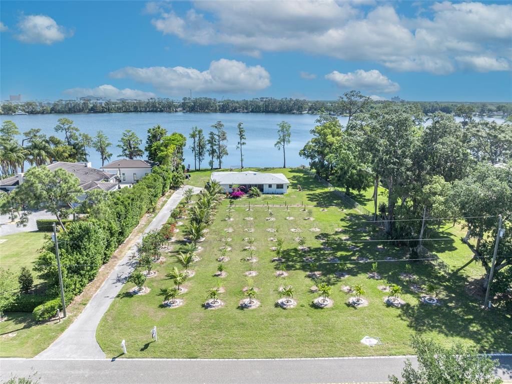 An aerial view shows a house on a large lot with many small trees near water — 7420 LAKE WILLIS DRIVE, ORLANDO, FL