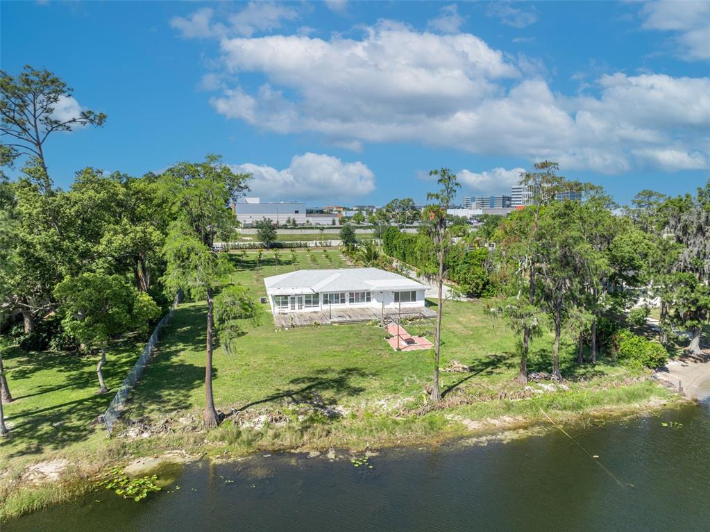 An aerial view of a white house with a deck situated on a grassy lakeshore — 7420 LAKE WILLIS DRIVE, ORLANDO, FL