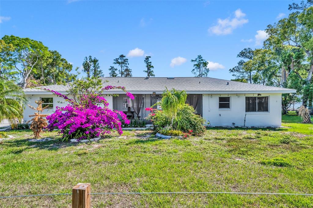 A single-story white house with a gray roof features a vibrant bougainvillea bush in front — 7420 LAKE WILLIS DRIVE, ORLANDO, FL