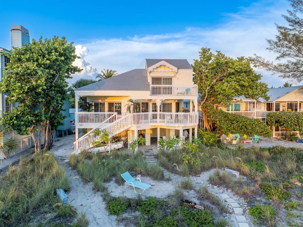 An elevated beach house with a white wrap-around porch and a sandy yard — 20052 GULF BOULEVARD, INDIAN SHORES, FL