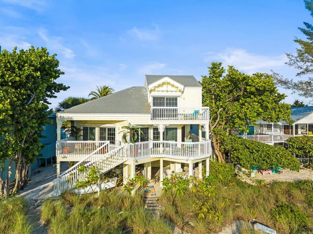 An elevated, light-yellow coastal house with a white wrap-around porch and a second-story balcony — 20052 GULF BOULEVARD, INDIAN SHORES, FL