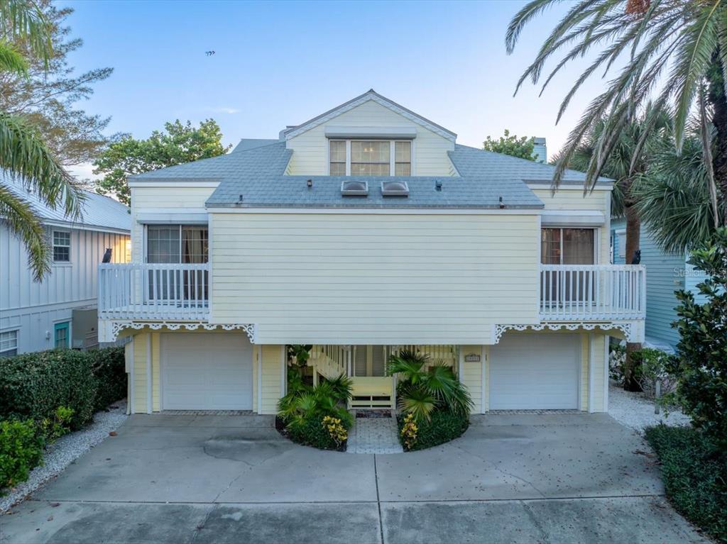 A two-story yellow house with two garage doors, balconies, and a paved driveway — 20052 GULF BOULEVARD, INDIAN SHORES, FL