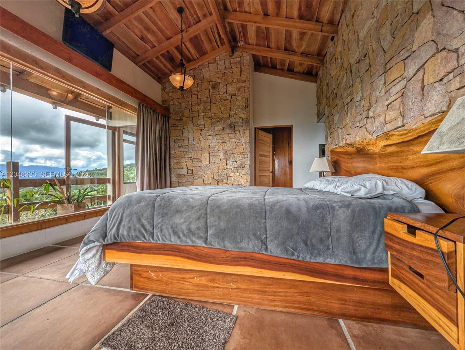 A bedroom features a stone wall, a wooden bed frame, and large windows with mountain views — 6 Cervantes Cartago Costa Rica, CR 00, CR