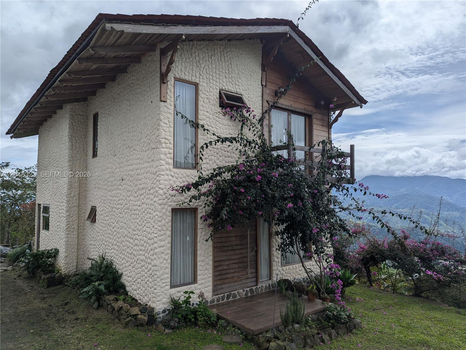 A two-story house with textured cream walls and a wooden balcony overlooks a mountain landscape — 6 Cervantes Cartago Costa Rica, CR 00, CR
