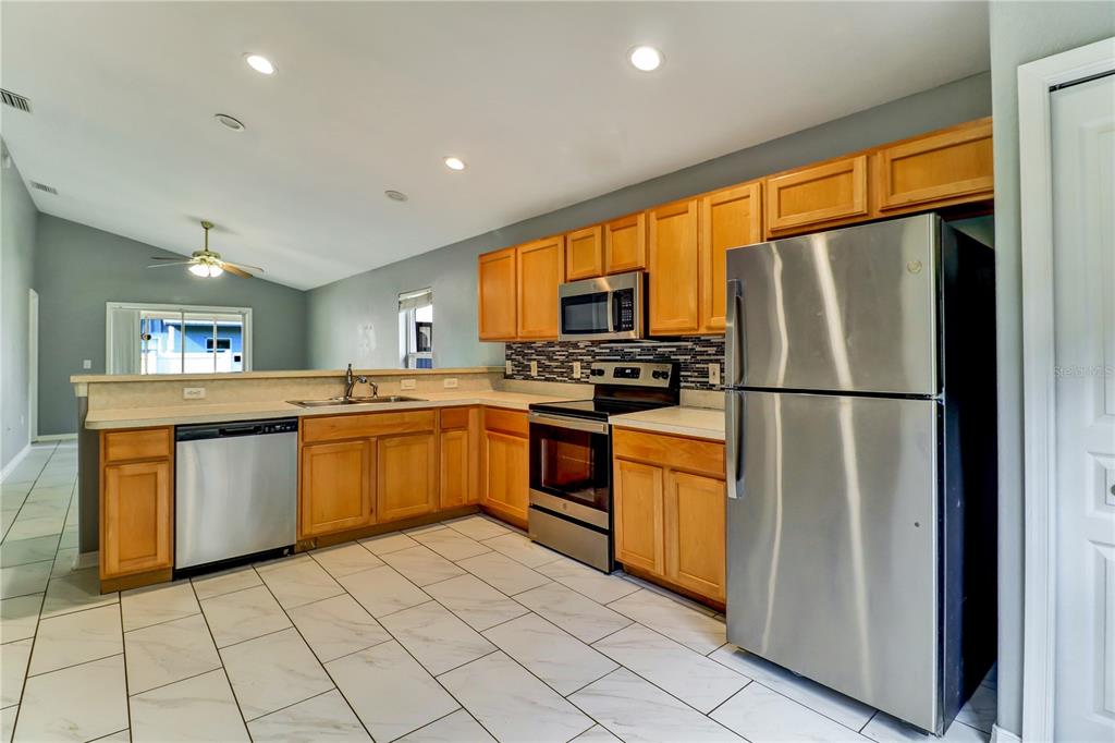 A kitchen features light wood cabinets, stainless steel appliances, and white tile flooring — 4305 MUTTER ROAD, ST CLOUD, FL