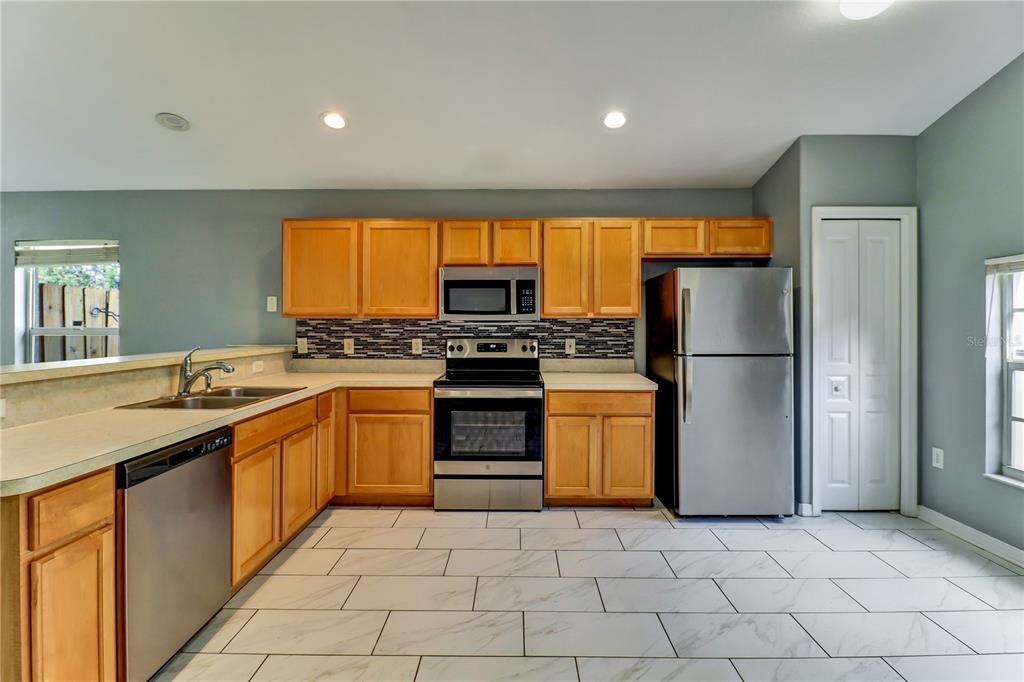 A kitchen with light wood cabinets, stainless steel appliances, and white marble-look tile flooring — 4305 MUTTER ROAD, ST CLOUD, FL