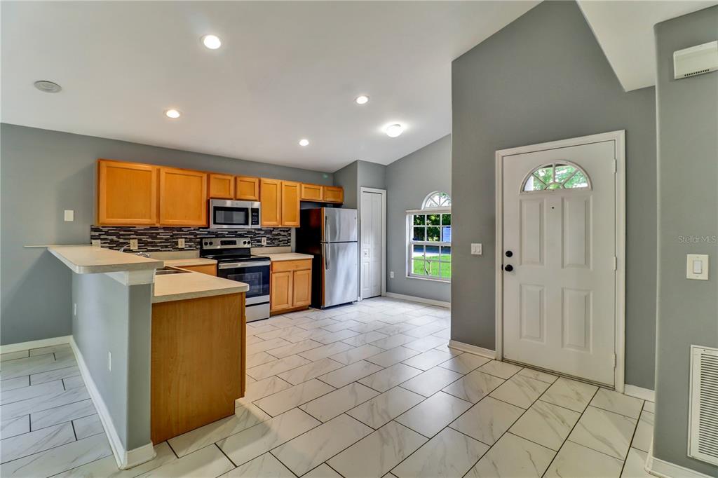 A kitchen with light wood cabinets, stainless steel appliances, and white tiled floors — 4305 MUTTER ROAD, ST CLOUD, FL