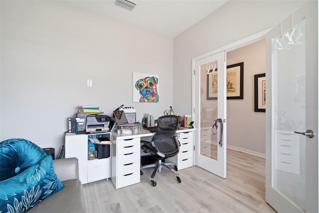 A home office features a white desk, a black mesh chair, and glass-paneled double doors — 31477 WESTBURY ESTATES AVENUE, WESLEY CHAPEL, FL