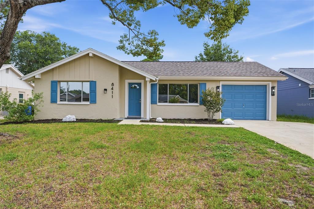 A single-story house with tan siding, blue shutters, a blue front door, and a garage — 8411 LINCOLNSHIRE DRIVE, HUDSON, FL