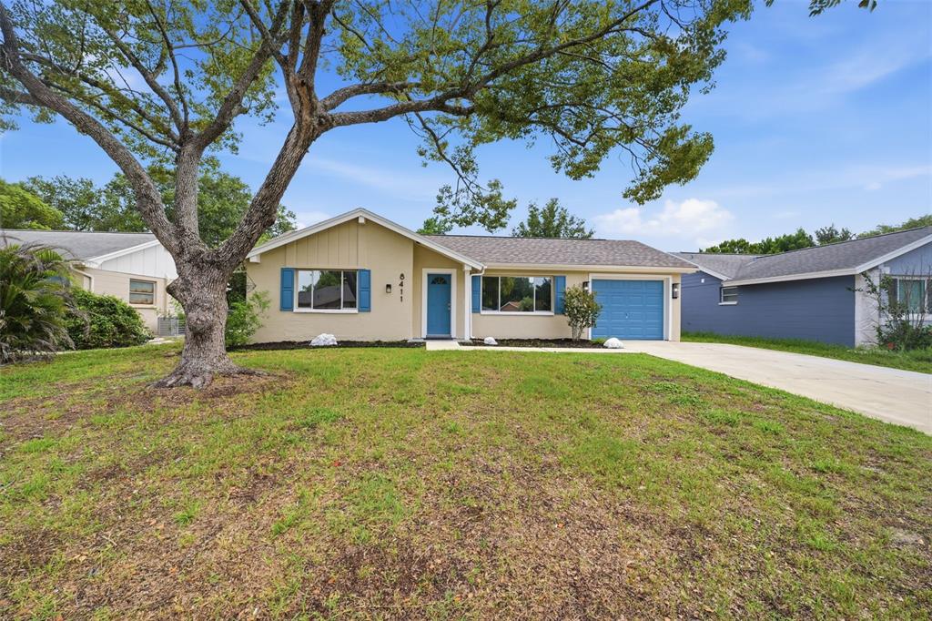 A single-story house with a tan exterior, blue shutters, and a front-facing garage — 8411 LINCOLNSHIRE DRIVE, HUDSON, FL
