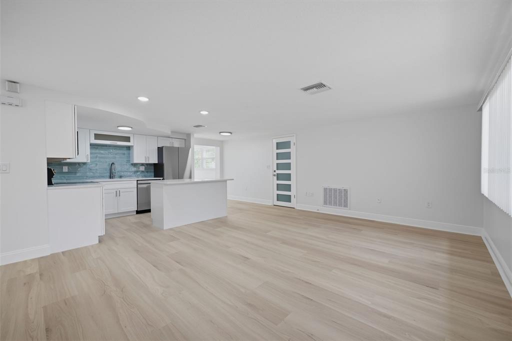 An open-concept kitchen and living area with white cabinetry, light wood flooring, and blue backsplash — 8411 LINCOLNSHIRE DRIVE, HUDSON, FL