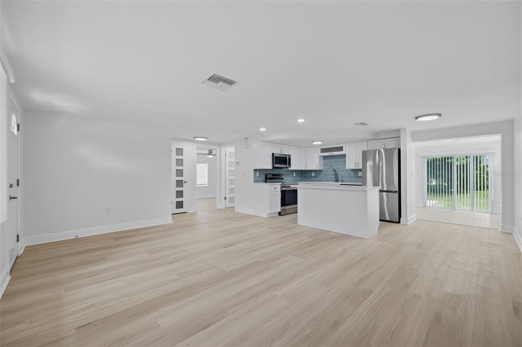An open-concept living area with light wood flooring, a white kitchen, and sliding glass doors — 8411 LINCOLNSHIRE DRIVE, HUDSON, FL